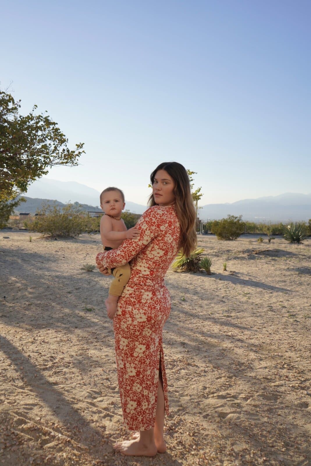 Ali Tate Cutler in a red floral dress holding her son, mountain landscape behind. Founder of Unfckwithable, the Instagram coaching brand for women.